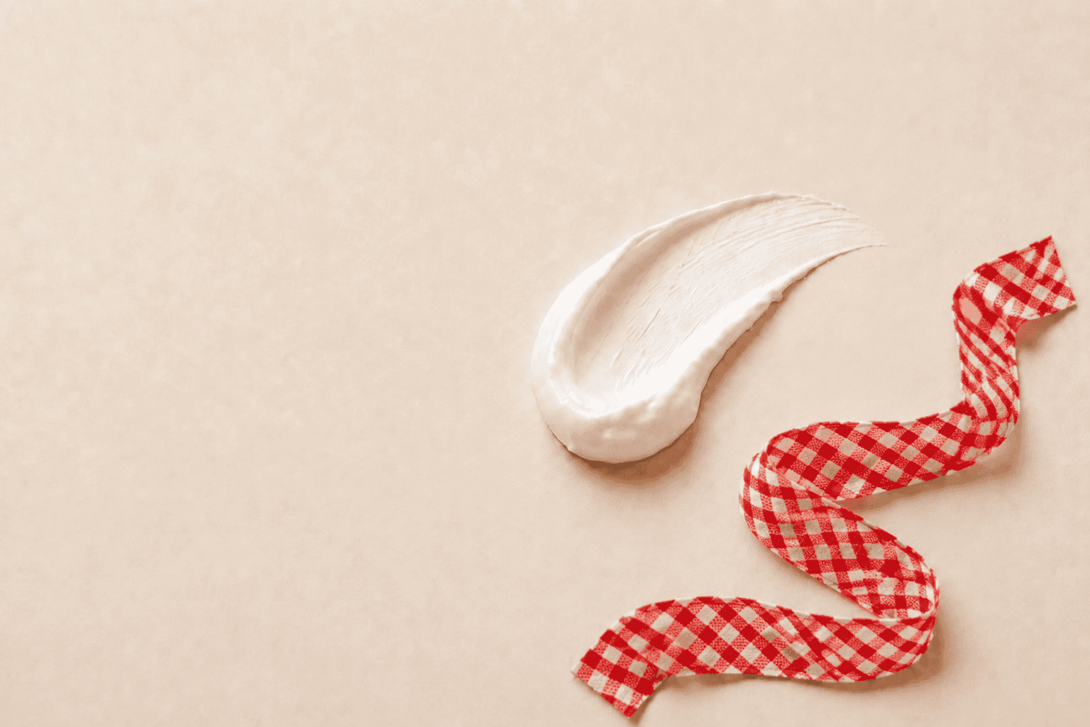 White moisturizing cream with flowing red-and-white gingham ribbon